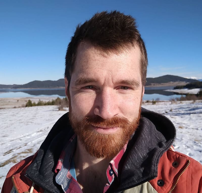 Scott Euser, smiling, in front of a snowy lake and hills